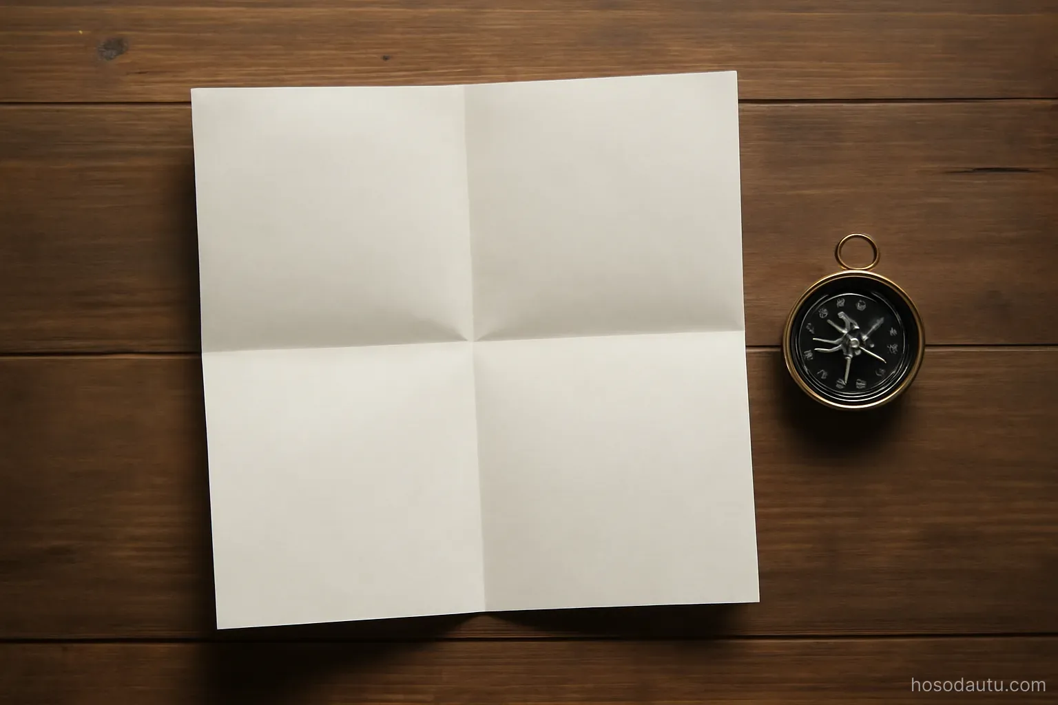a folded paper map lying open on a table with a compass beside it, overhead view, map surface blank and unmarked