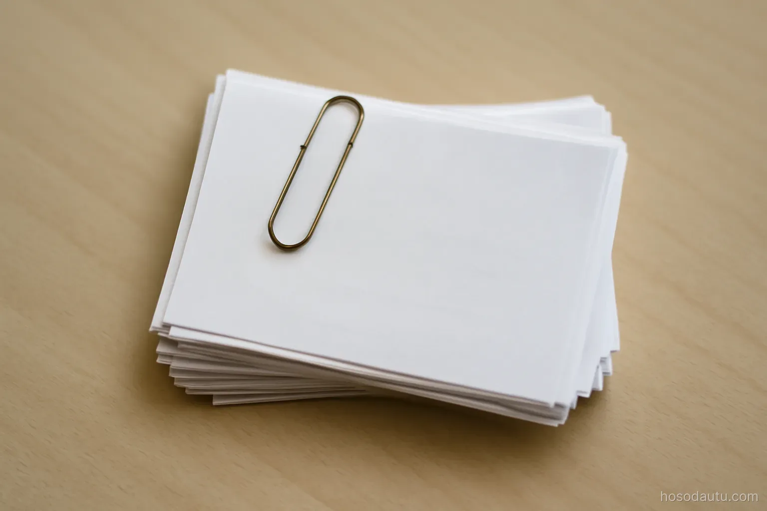 a stack of bank slips held together with a paper clip on a plain desk, close overhead view, print not legible